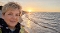 Frau mit kurzem blondem Haar und schwarzem Schal am Strand bei Sonnenuntergang