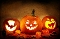 Drei leuchtende Halloween-Kürbisse mit geschnitzten Motiven Fledermaus, grinsendes Gesicht und schwarze Katze auf Herbstlaub